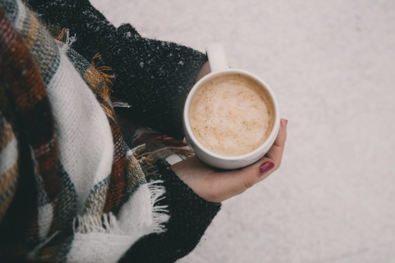 person in scarf holding mug of hot drink